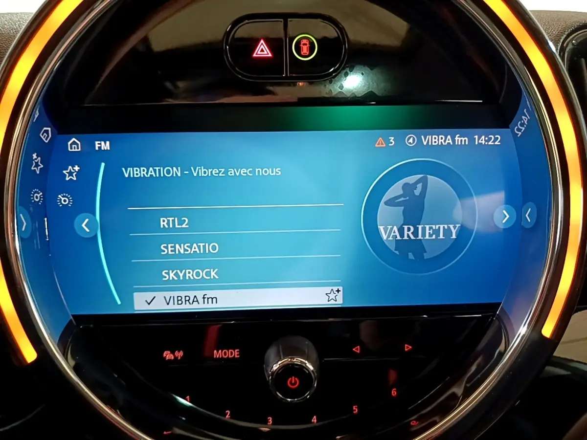 Gros plan sur l'écran tactile central rond du MINI Countryman gris clair, avec ambiance lumineuse orange autour.