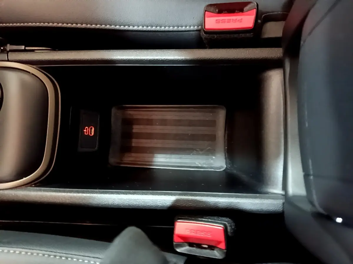 Vue plongeante sur la console centrale noire du MINI Countryman gris clair, avec zone de recharge par induction et boutons de ceinture rouges.