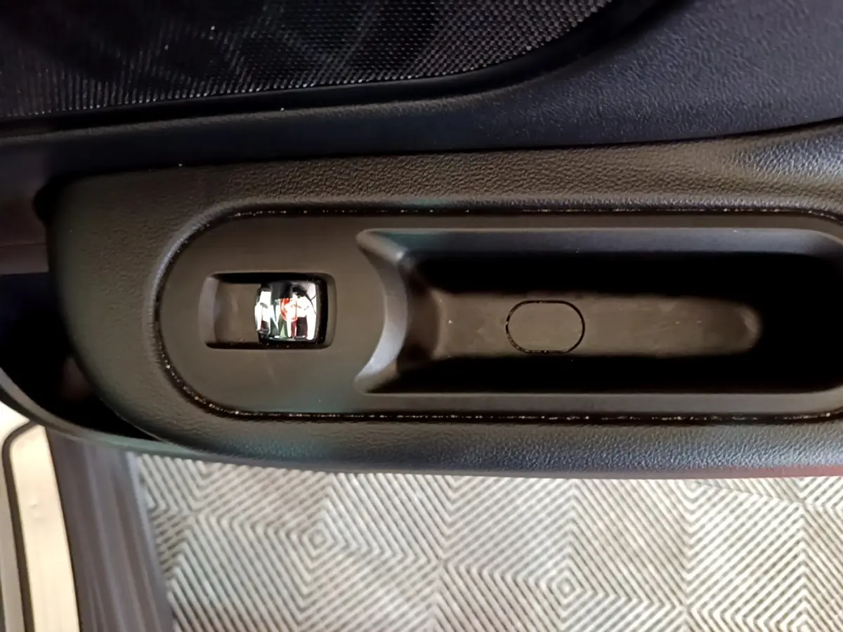 Poignée intérieure de porte noire vue de dessus sur MINI Countryman gris clair, avec bouton de verrouillage intégré.