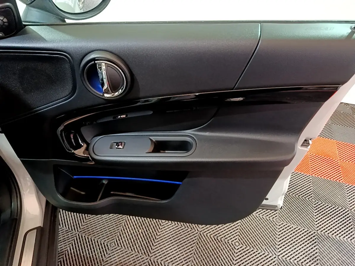 Vue intérieure de la porte avant gauche d'une MINI Countryman 2022 avec éclairage d'ambiance bleu et garniture noire.