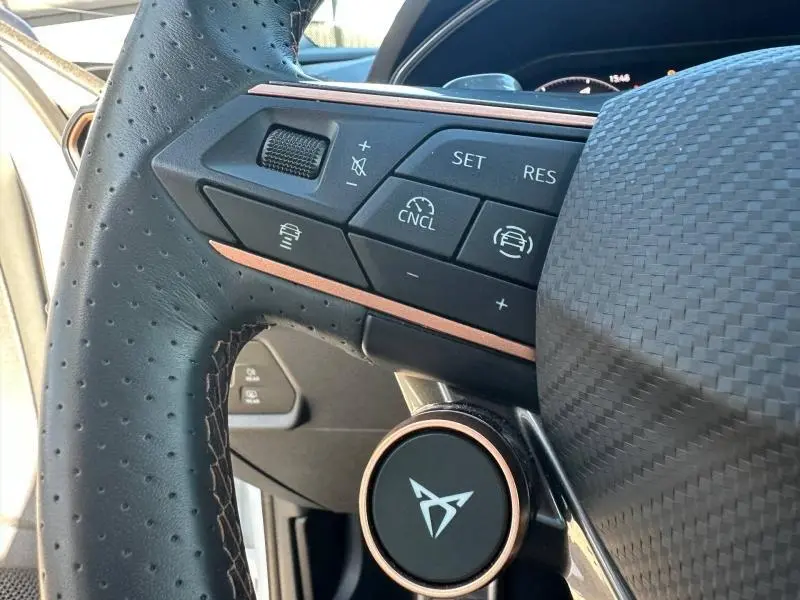 Gros plan sur la partie gauche du volant perforé noir avec commandes et logo CUPRA en finition cuivre.