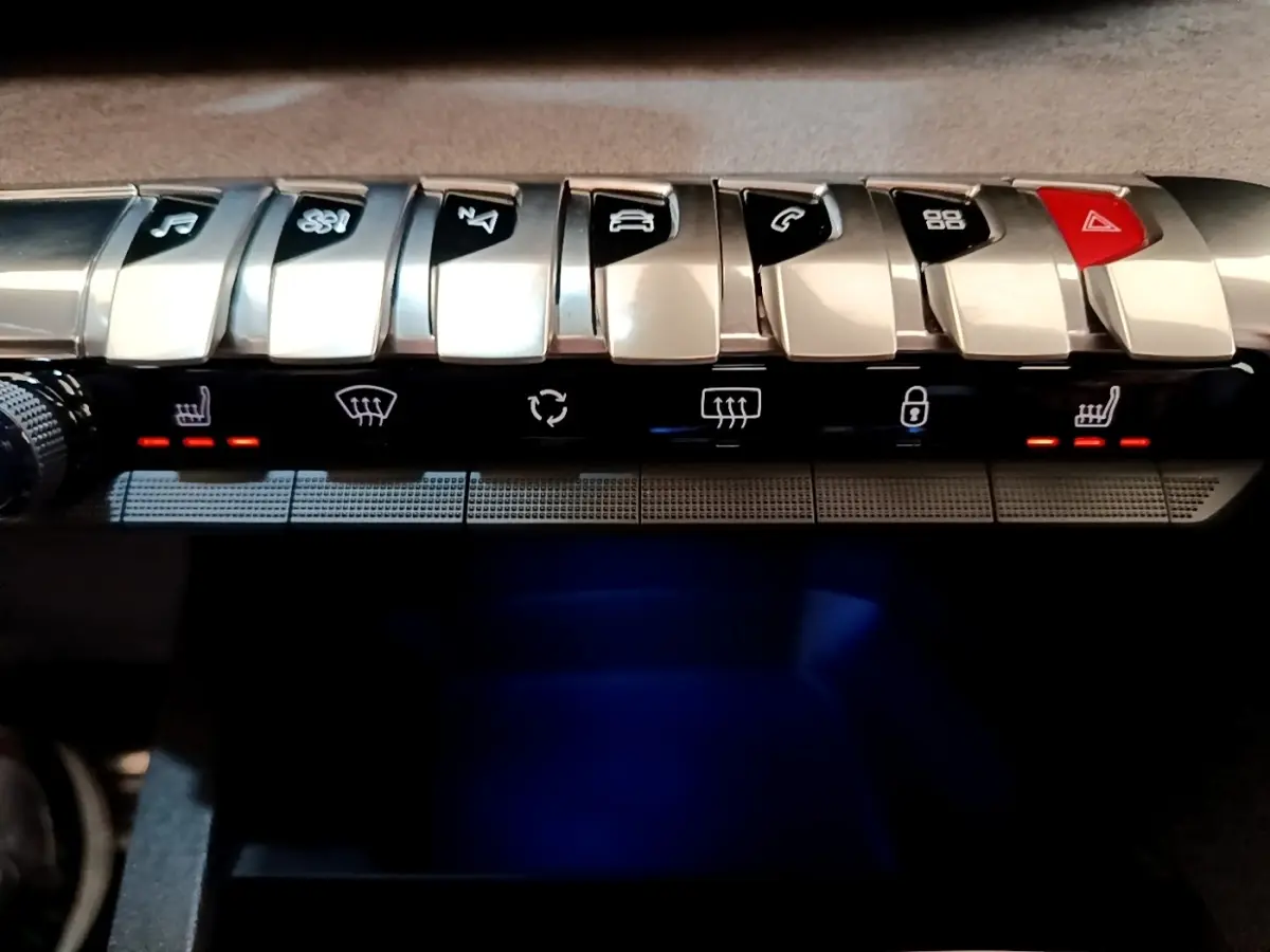 Gros plan sur la rangée de boutons argentés du tableau de bord du Peugeot 3008 noir, avec éclairage rouge des sièges chauffants.