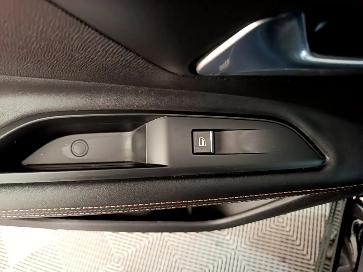 Détail de la commande de lève-vitre côté conducteur en plastique noir avec couture orange sur la porte intérieure du Peugeot 3008 noir.