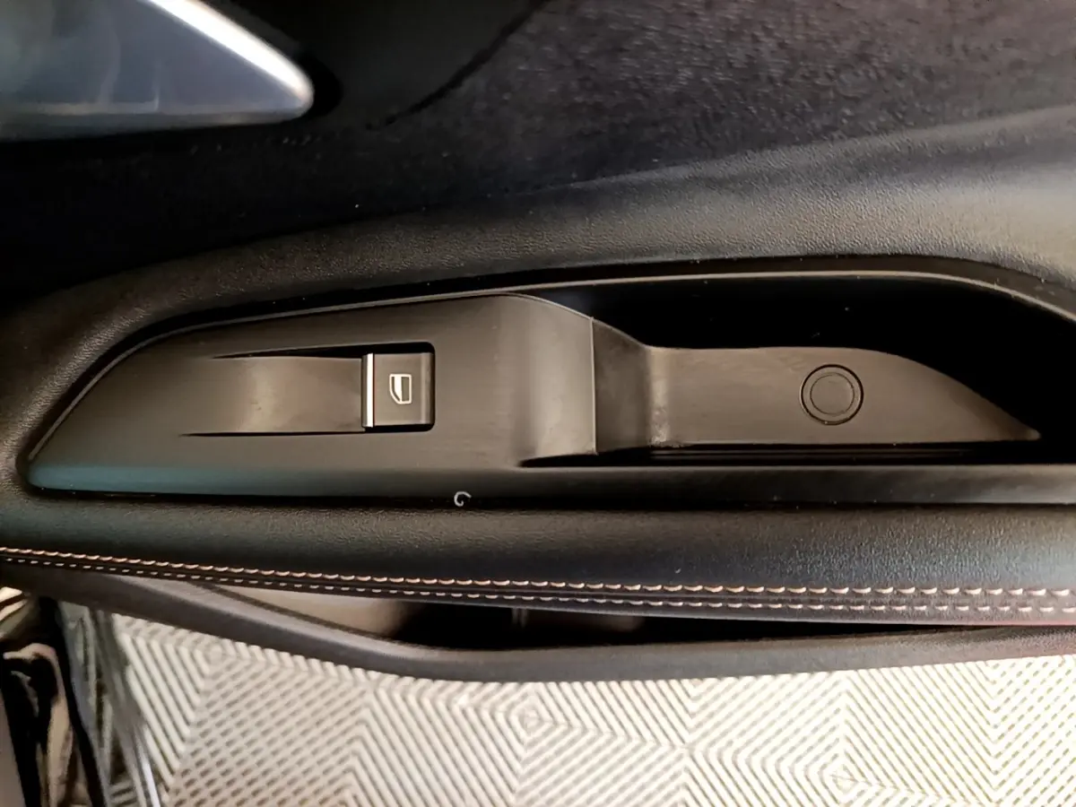 Détail de la commande de lève-vitre côté gauche en plastique noir avec surpiqûres contrastantes sur la porte d’un Peugeot 3008 noir.