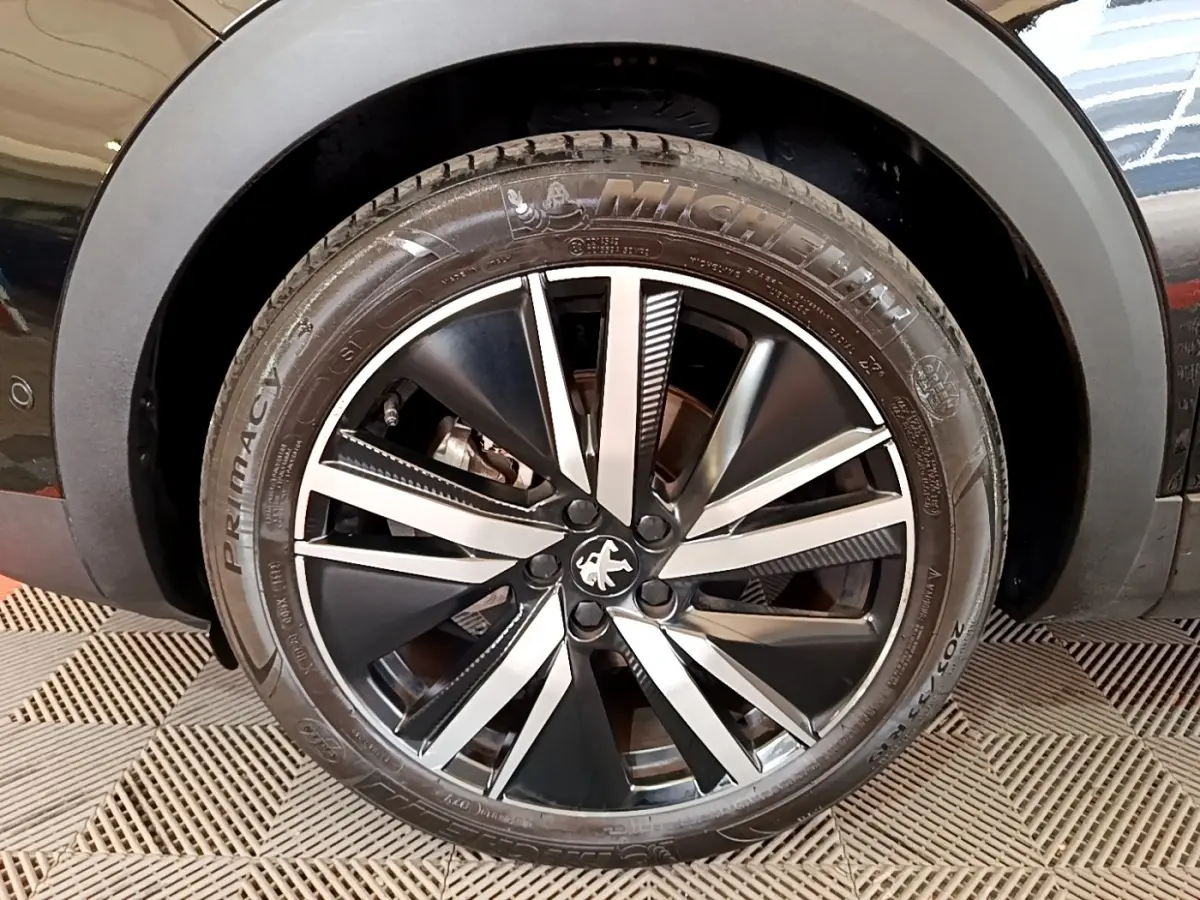 Gros plan sur la jante alliage noire et argentée d’un Peugeot 3008 noir, avec pneu Michelin visible.