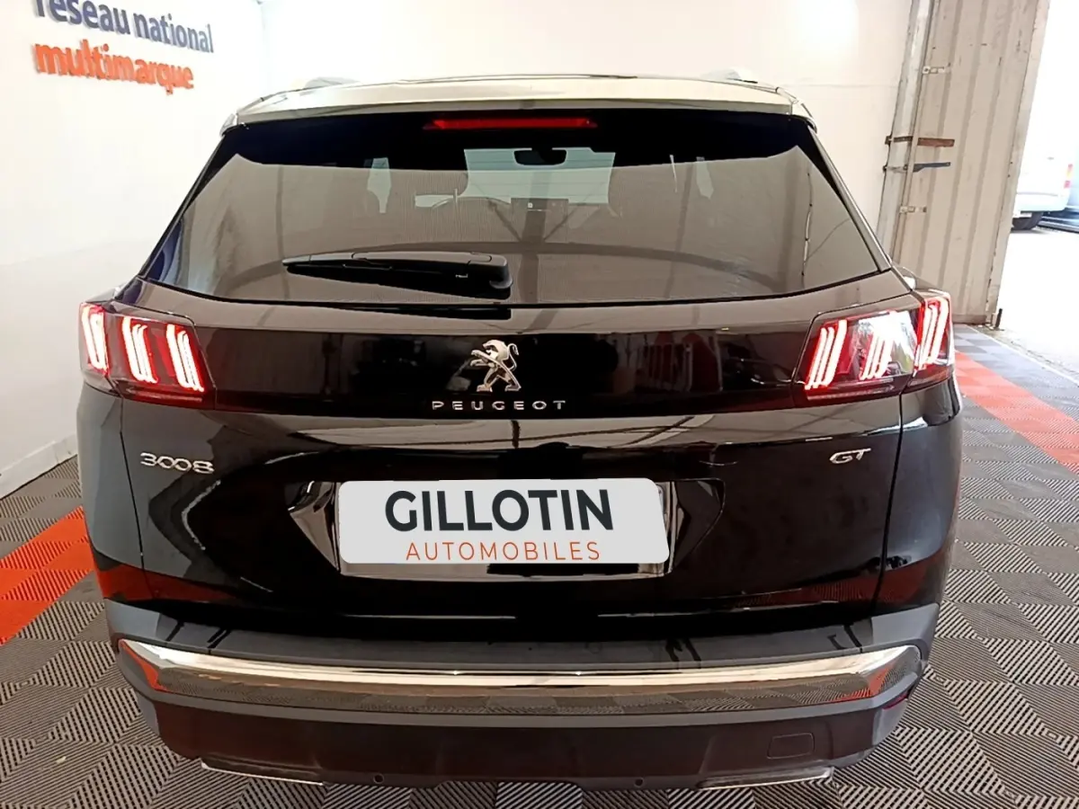 Vue arrière d'un Peugeot 3008 noir version GT Pack avec feux LED caractéristiques allumés en intérieur showroom.