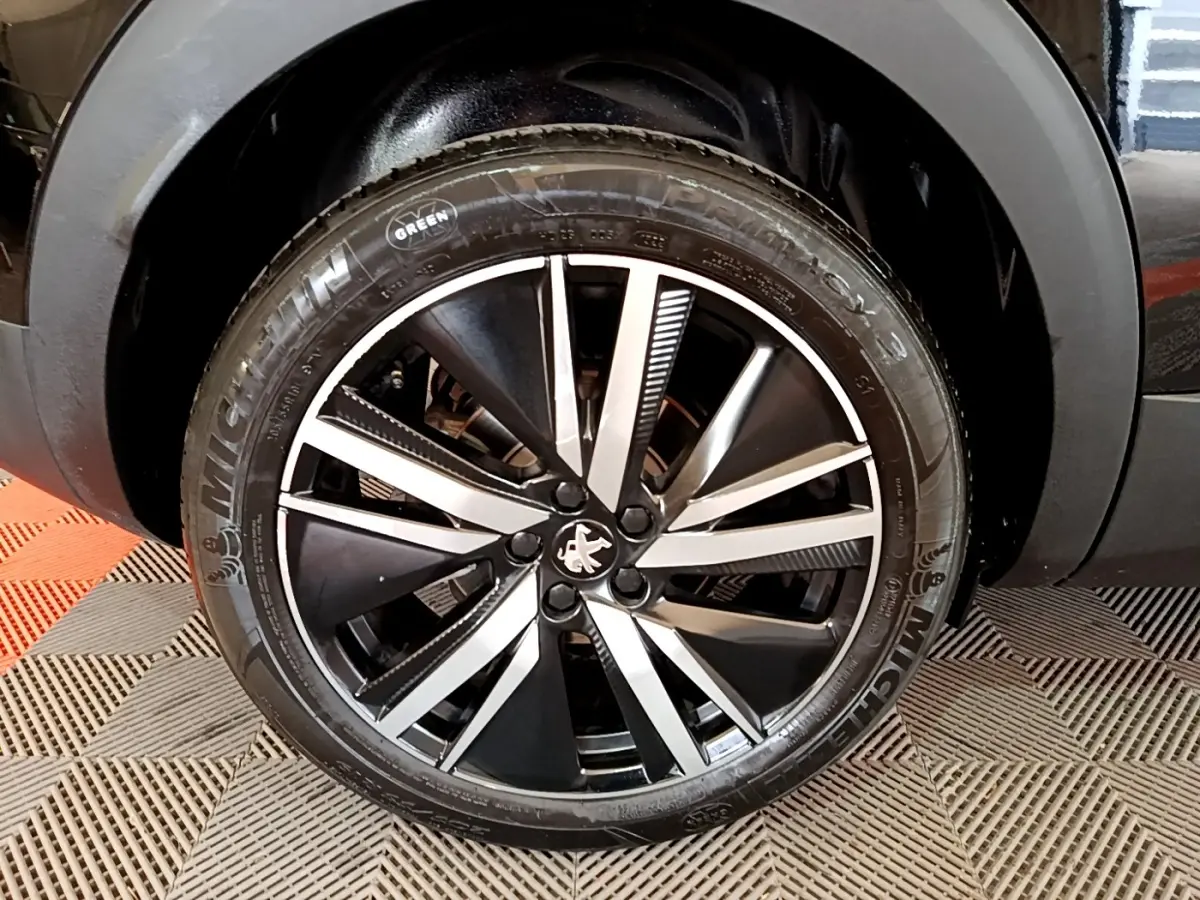 Gros plan sur la jante alliage noir et argent avec logo Peugeot, roue avant droite du 3008 noir 2022.