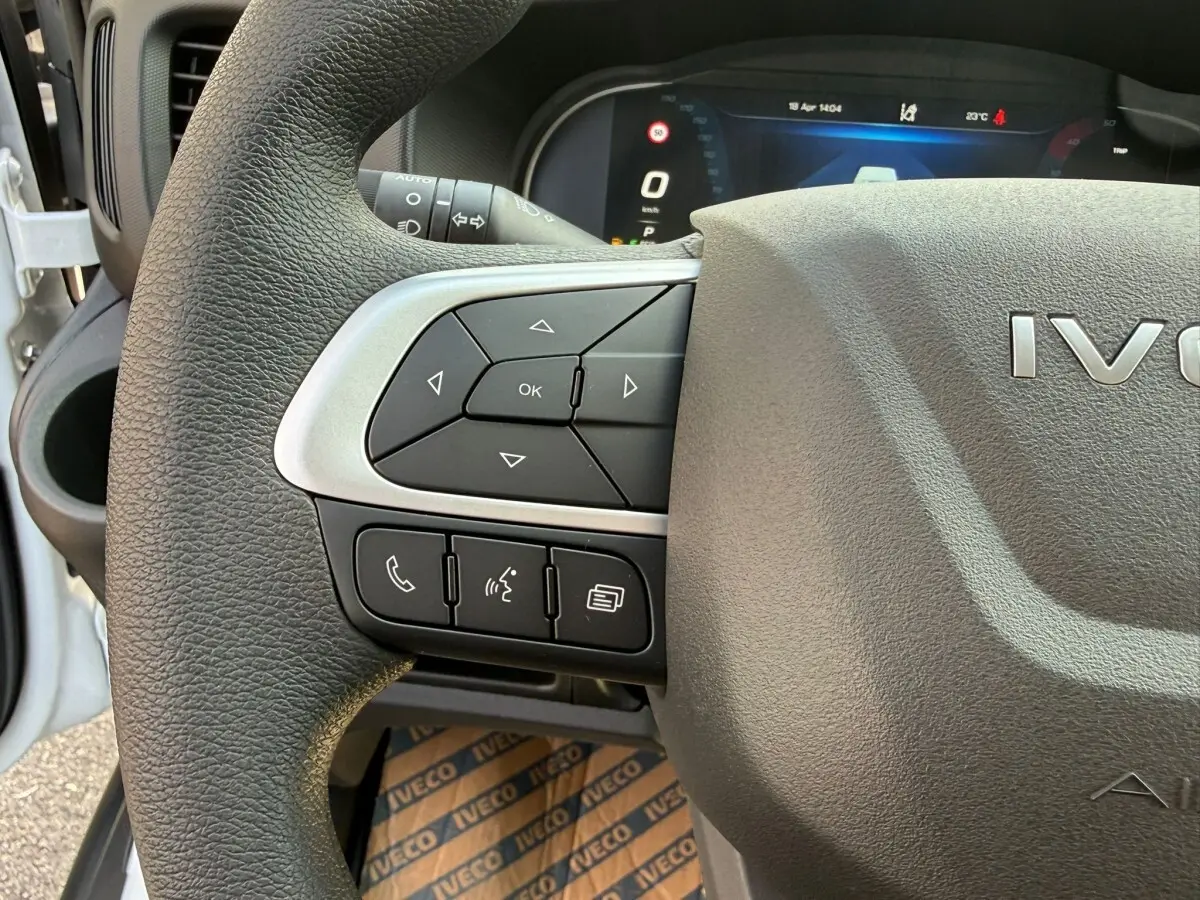 Gros plan sur le volant côté gauche de l'IVECO Daily blanc 2026, avec commandes multifonctions et tableau de bord numérique visible.