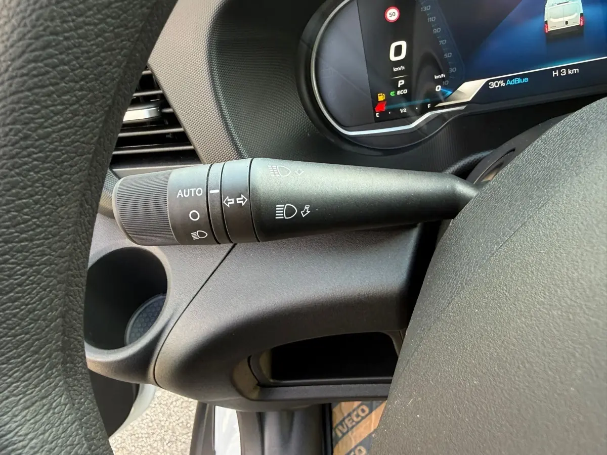Gros plan sur la manette des phares et clignotants à gauche du volant dans l’habitacle du Iveco Daily blanc 2026.