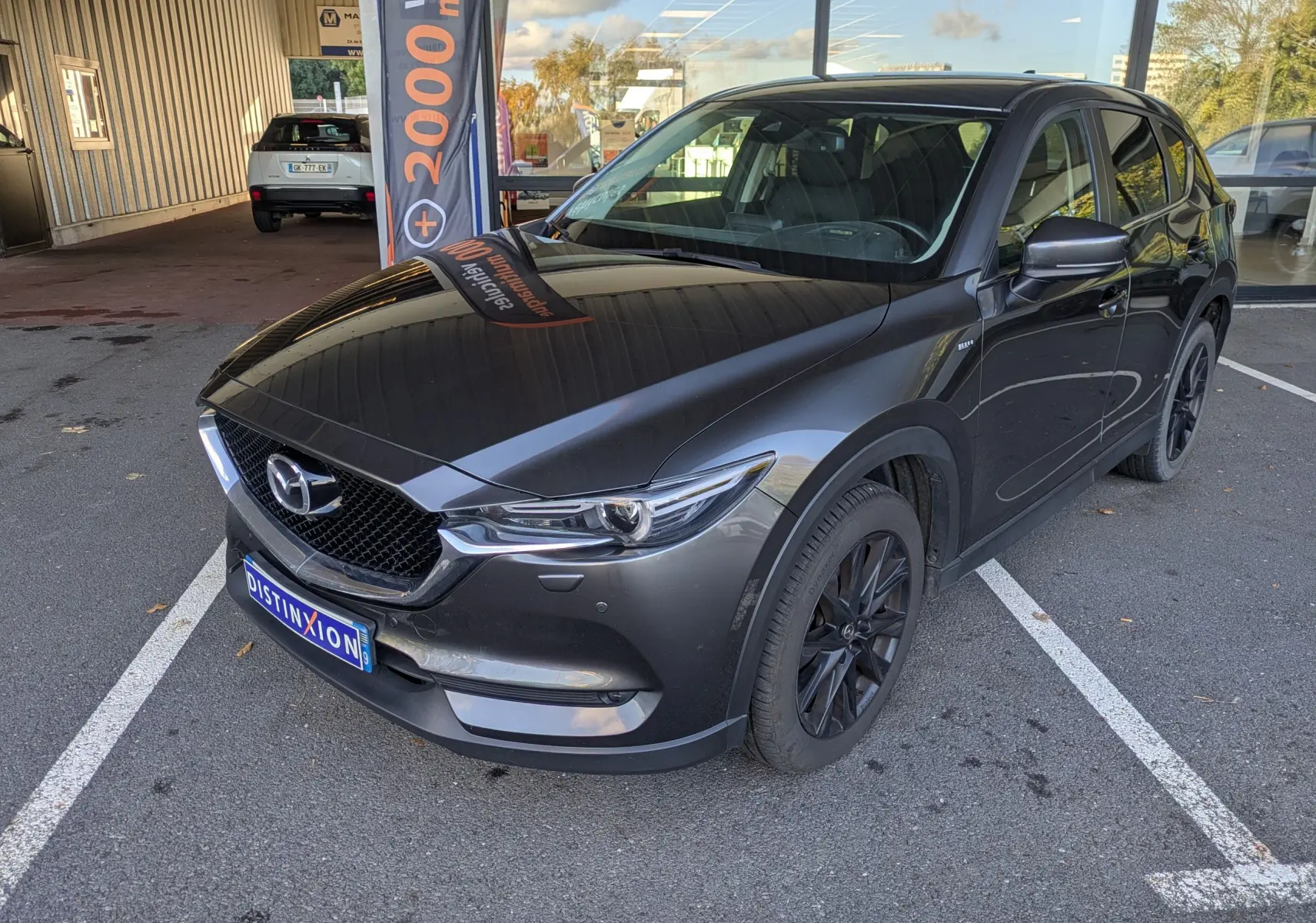 Vue de profil côté gauche d'un Mazda CX-5 gris 2020 avec jantes noires et badge SKYACTIV-D visible sur l'aile avant.