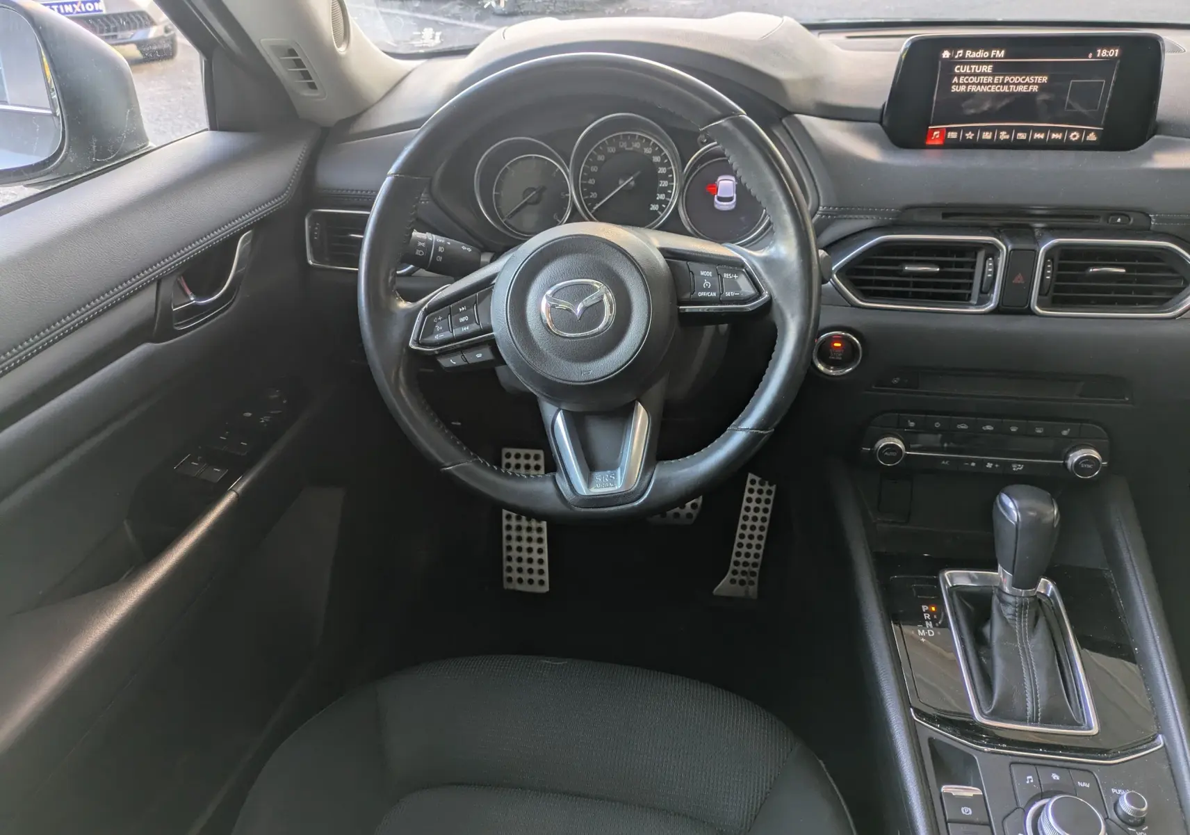 Vue intérieure du poste de conduite du Mazda CX-5 gris 2020, avec volant multifonctions et écran central tactile.