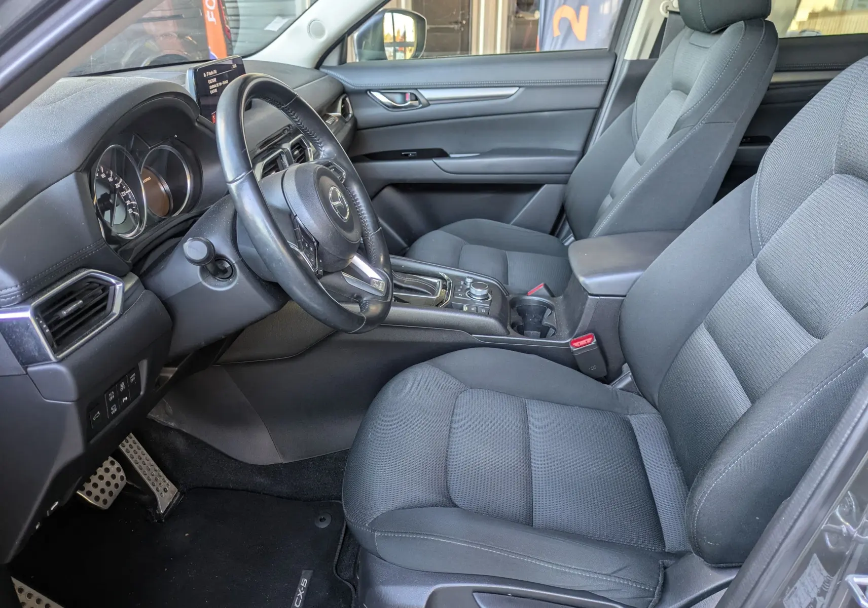 Intérieur avant droit du Mazda CX-5 gris 2020, sièges tissu noirs et console centrale avec boîte automatique visible.