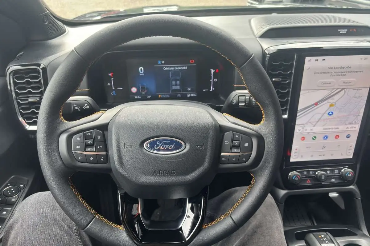 Vue intérieure centrée sur le volant cuir noir avec surpiqûres orange et écran tactile vertical du Ford Ranger Wildtrak 2026.
