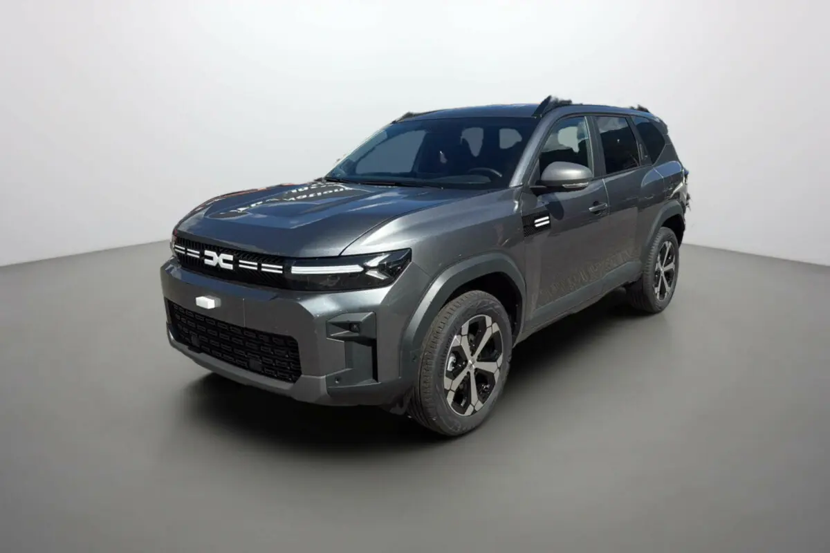 SUV Dacia Bigster gris schiste en 3/4 avant droit, avec jantes alu 18 pouces et barres de toit noires.