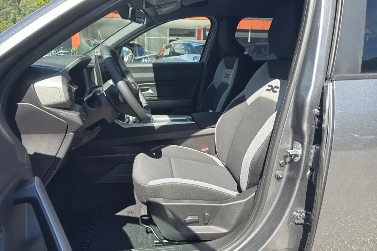 Intérieur côté conducteur du Dacia Bigster gris schiste 2025, sièges tissu avec logo X et volant cuir.
