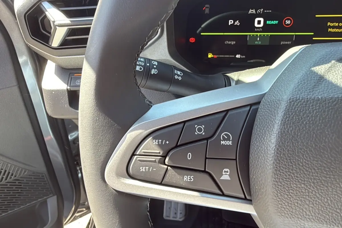 Gros plan sur les commandes au volant cuir du Dacia Bigster gris schiste, avec tableau de bord digital en arrière-plan.