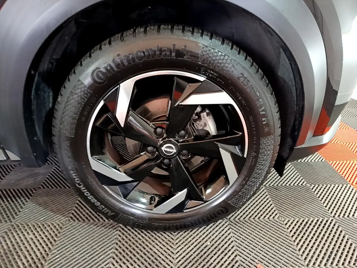 Gros plan sur la roue avant droite du Nissan Juke Hybrid 143 Business+ noir avec jante alliage noire et argentée.