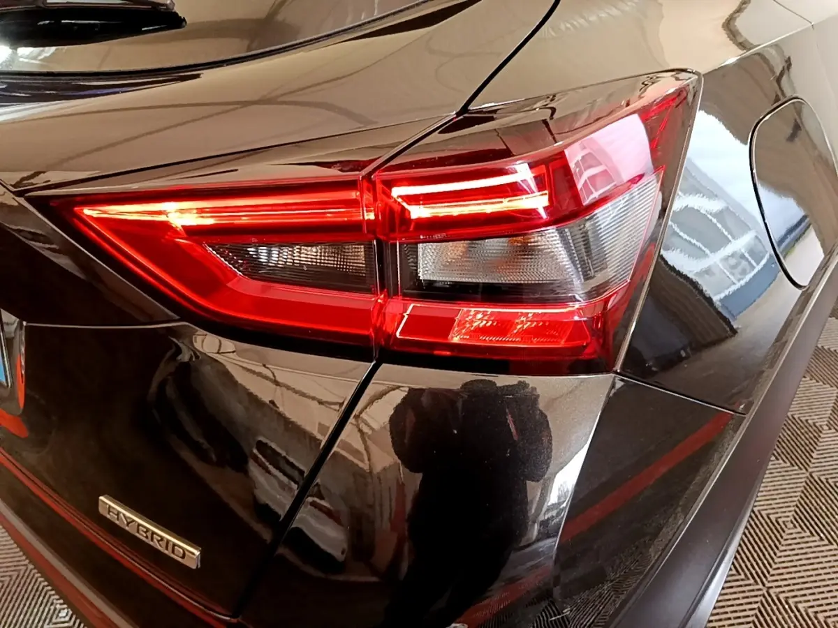 Gros plan sur le feu arrière droit rouge et blanc d’un Nissan Juke Hybrid noir brillant avec badge Hybrid visible.