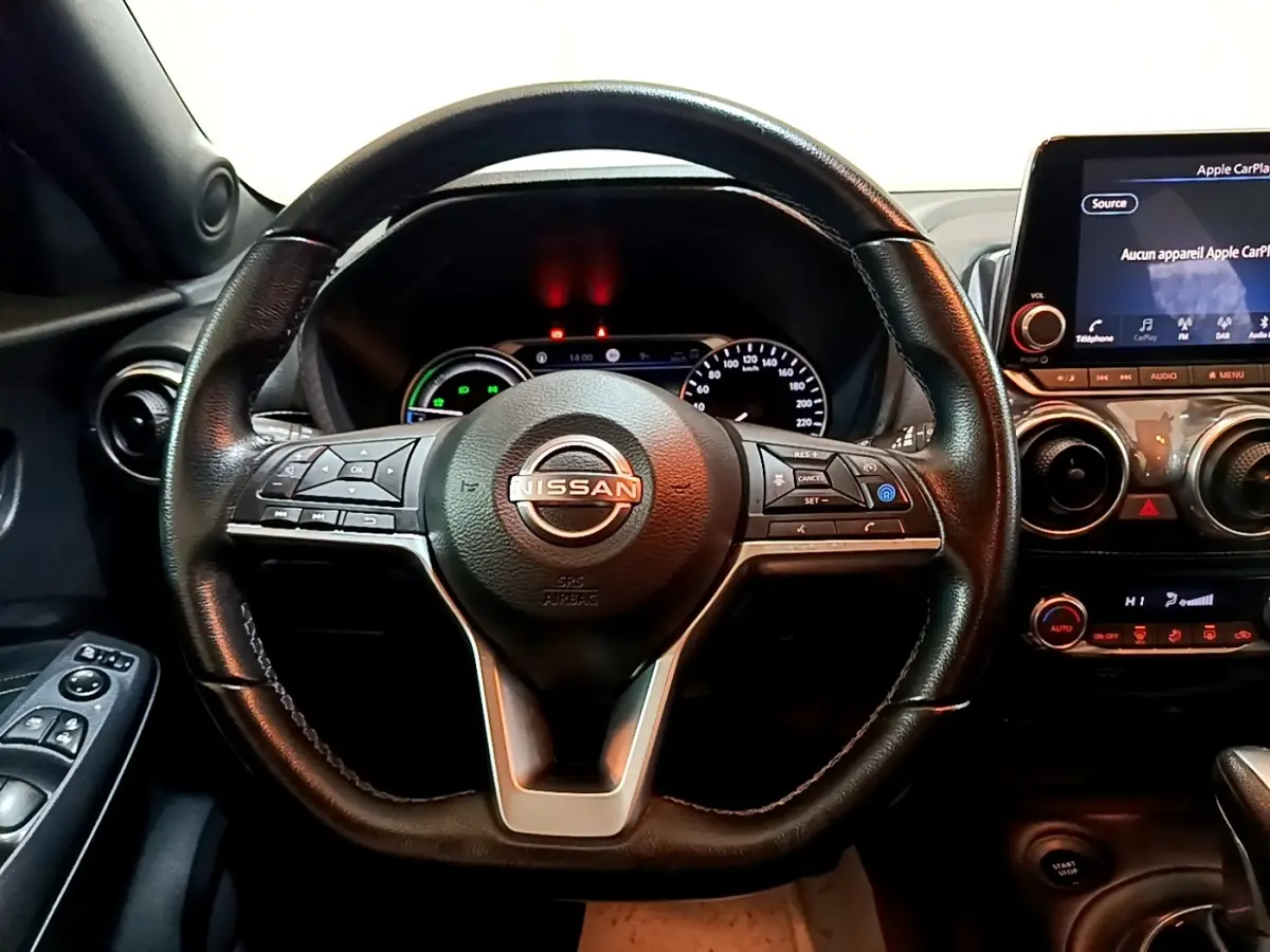 Vue intérieure centrée sur le volant cuir noir du Nissan Juke Hybrid 2022 avec tableau de bord et écran tactile visible.