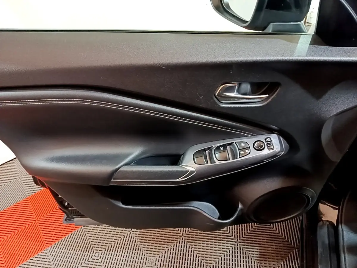 Vue intérieure du côté gauche de la porte avant noire du Nissan Juke Hybrid 143 Business+ avec commandes de vitres et rétroviseur.