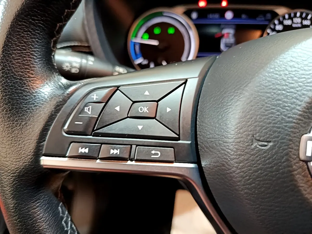 Gros plan sur les commandes gauche du volant cuir noir du Nissan Juke Hybrid 143 Business+ 2022 avec tableau de bord en arrière-plan.