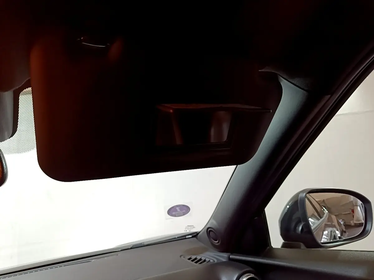 Vue intérieure côté conducteur du Nissan Juke Hybrid 143 Business+ noir, avec pare-soleil et rétroviseur extérieur visible.