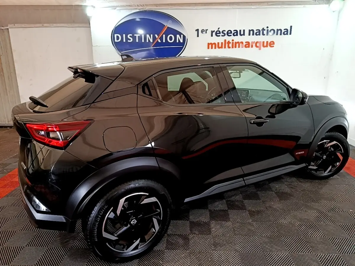 Vue 3/4 arrière droite d'un Nissan Juke Hybrid 143 Business+ noir brillant avec jantes noires et logo Hybrid visible.