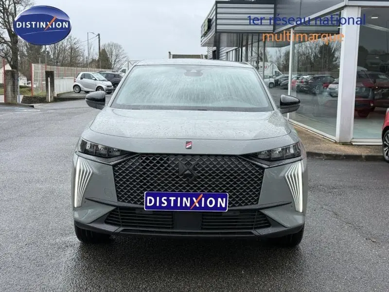 Vue avant d'un DS7 E-TENSE gris 2024 avec calandre noire et feux LED verticaux allumés sur parking humide.