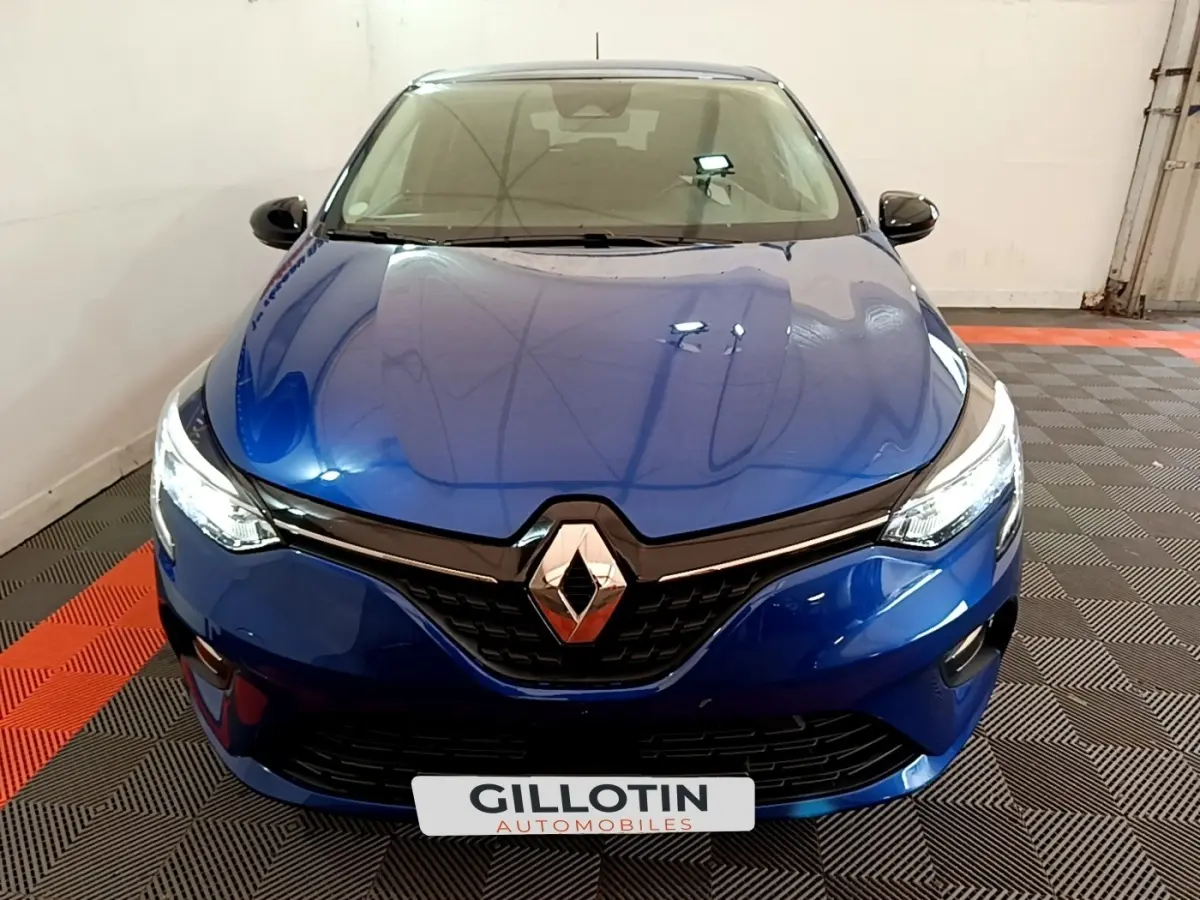 Vue frontale d'une Renault Clio Evolution bleu électrique avec phares LED allumés dans un garage.