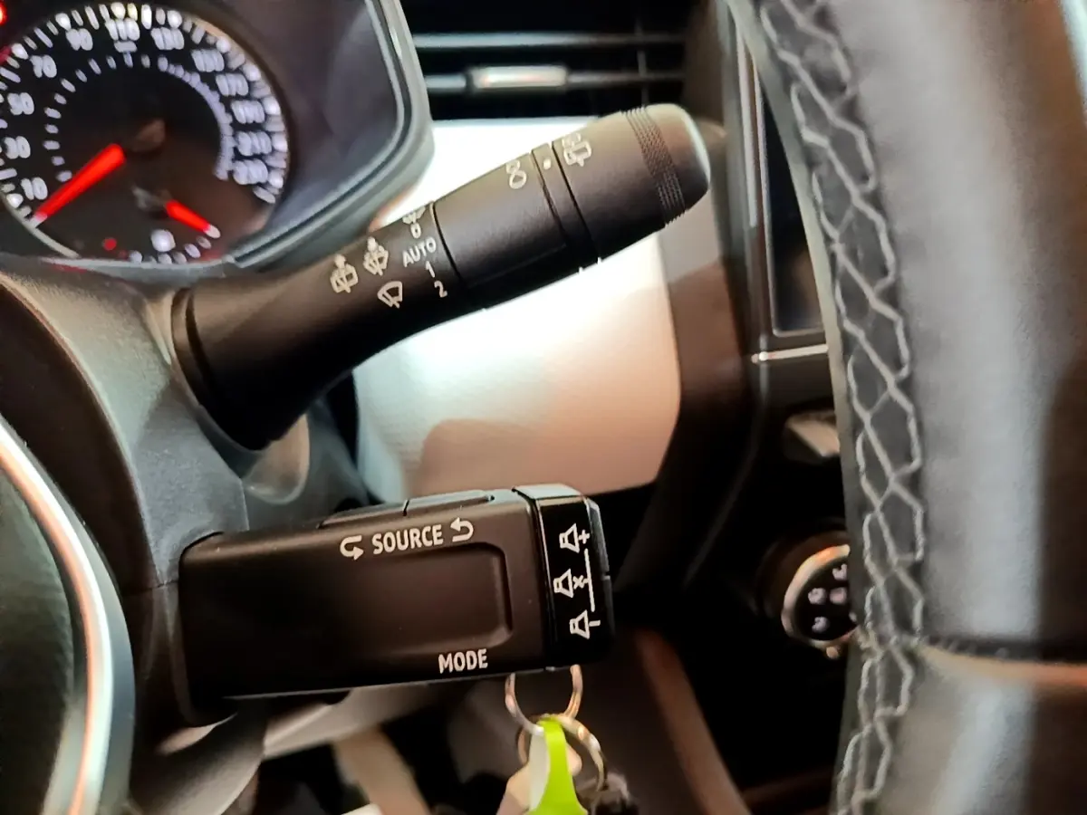 Gros plan sur la commande multimédia au volant cuir noir de la Renault Clio bleu, avec tableau de bord partiellement visible.