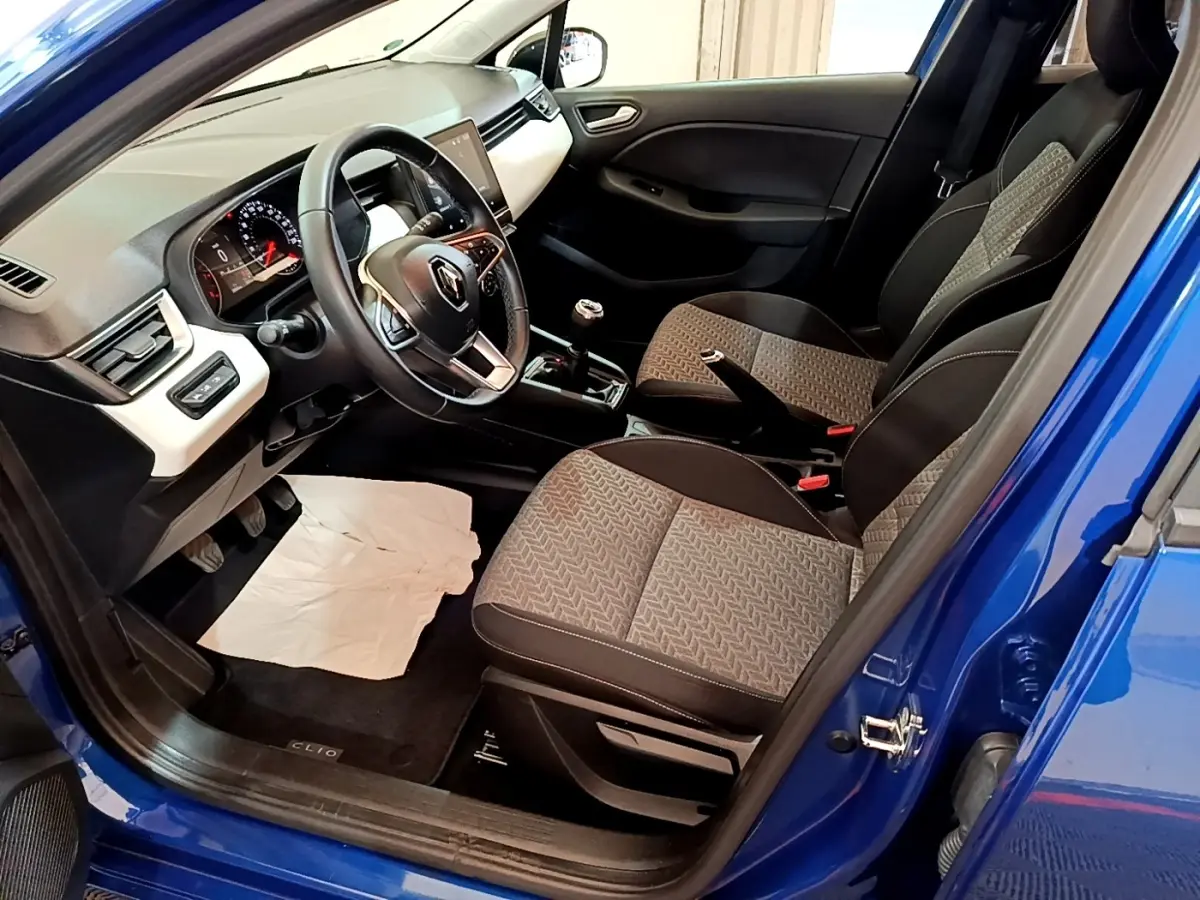 Vue intérieure côté conducteur d’une Renault Clio bleu 2022, volant cuir multifonctions et sièges tissu gris à motifs.