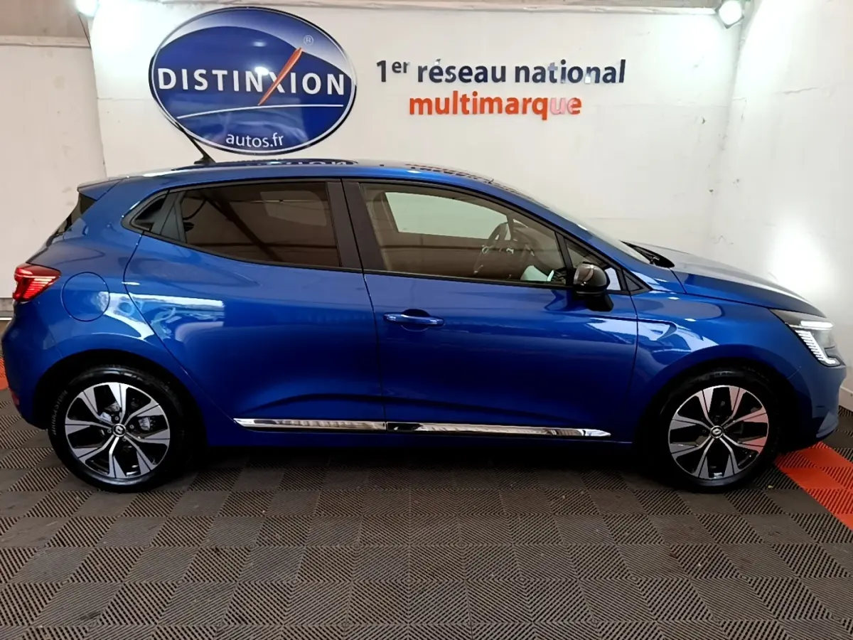 Profil droit d'une Renault Clio bleu 2022 avec jantes alliage et vitres teintées, dans un showroom intérieur.