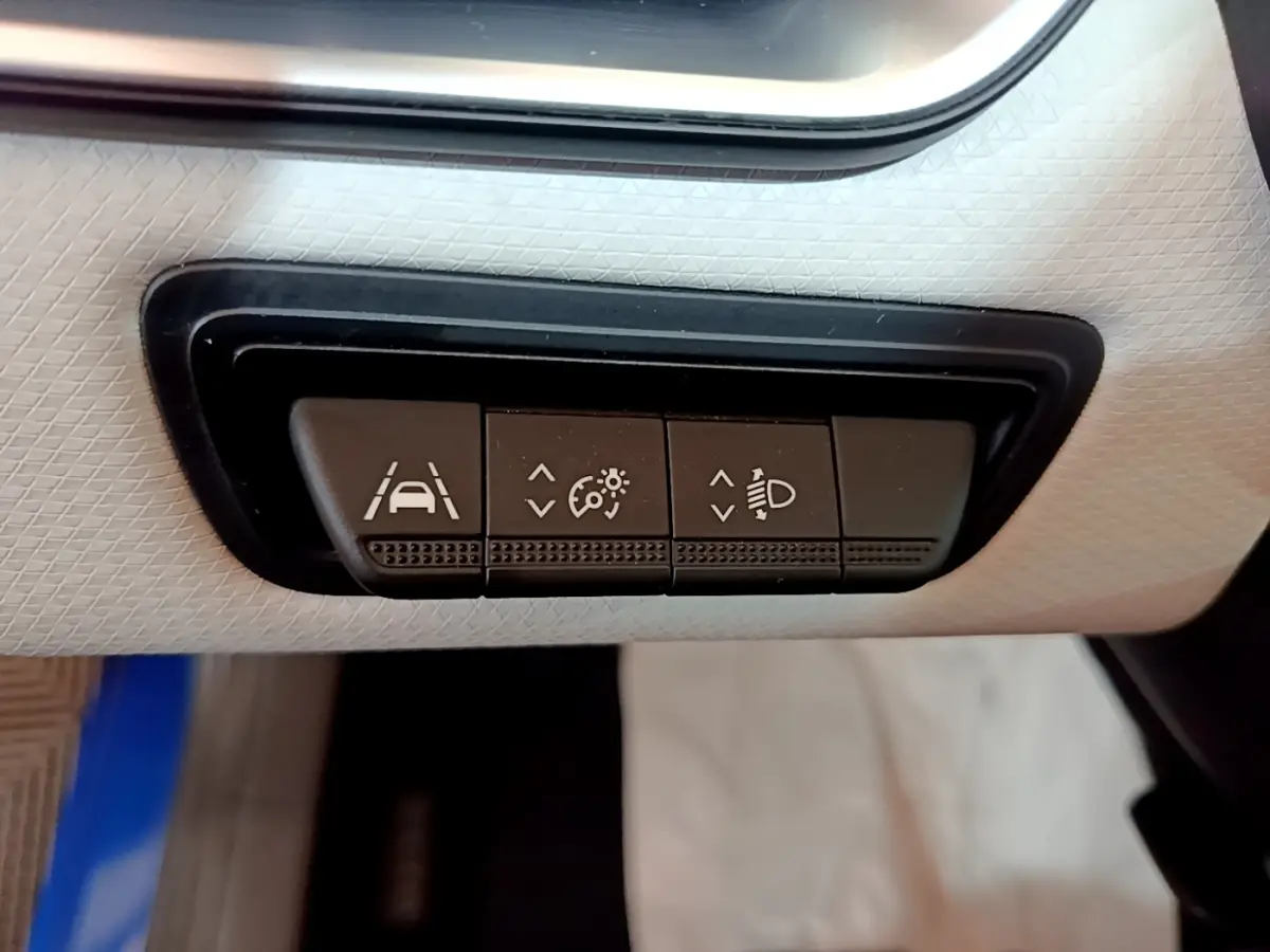 Gros plan sur les boutons de réglage des aides à la conduite dans une Renault Clio bleu, intérieur clair.