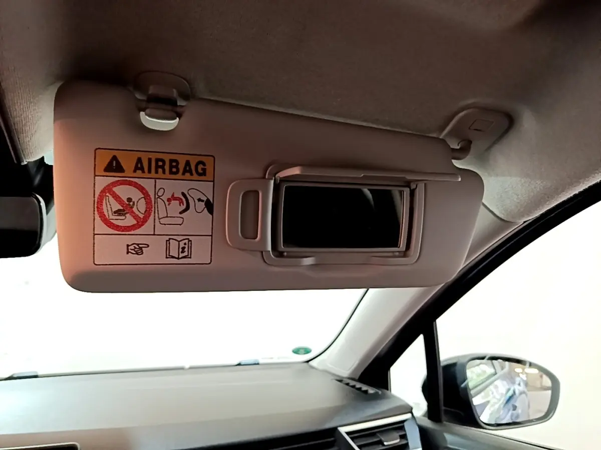 Intérieur de la Renault Clio Evolution bleu, vue côté passager sur pare-soleil avec miroir et avertissement airbag.