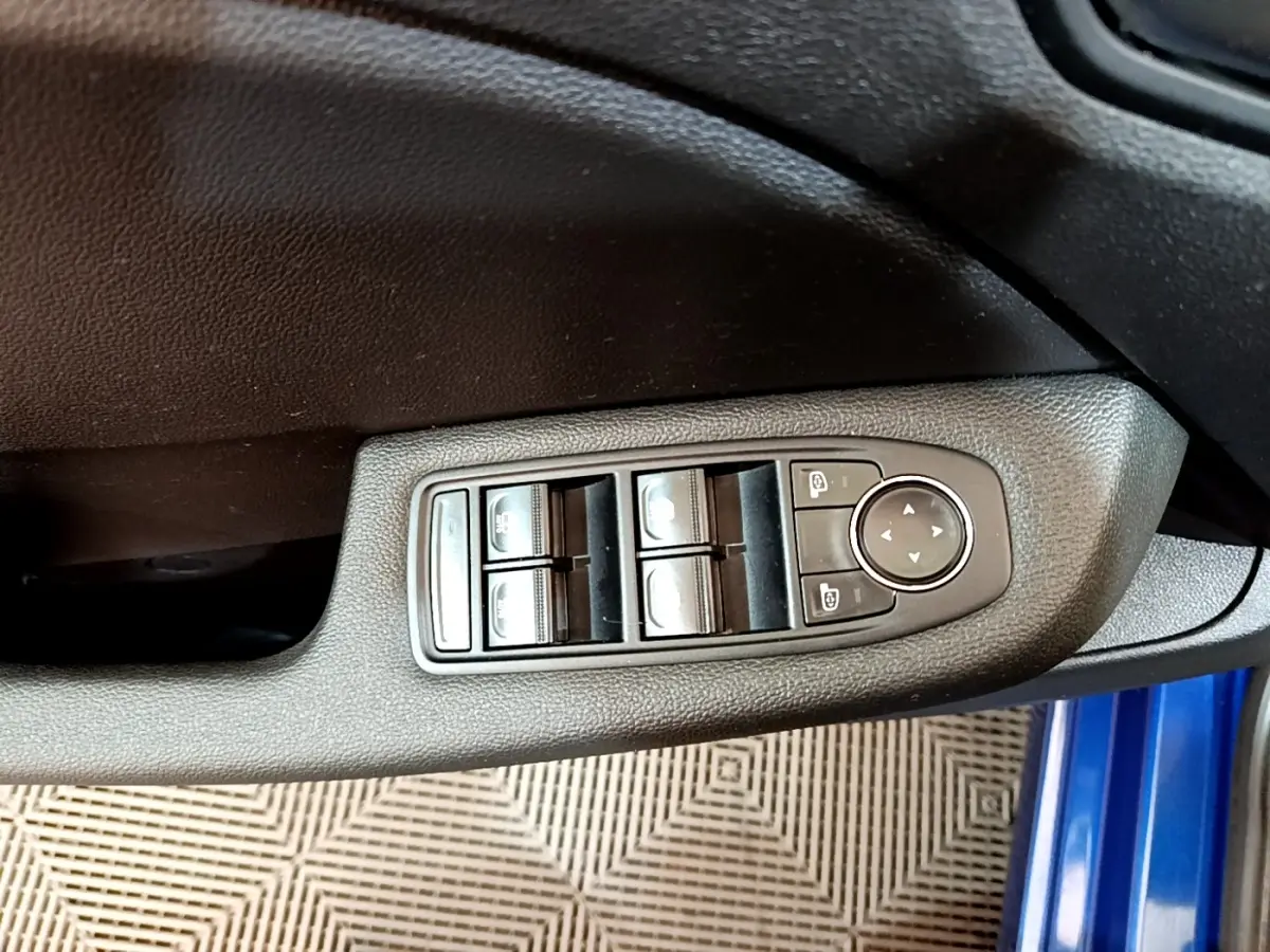 Gros plan sur les commandes de lève-vitres et réglage des rétroviseurs côté conducteur d’une Renault Clio bleu 2022.