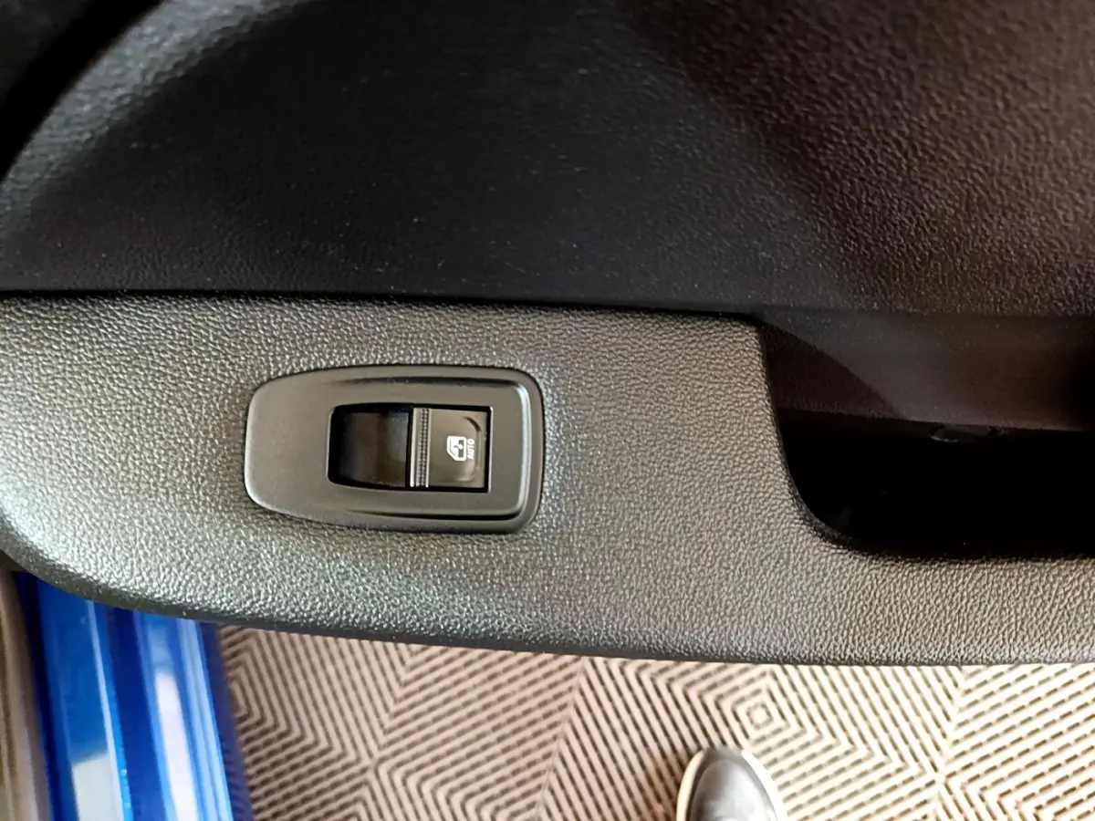 Gros plan sur le bouton de commande de la vitre électrique côté conducteur d'une Renault Clio bleu 2022.