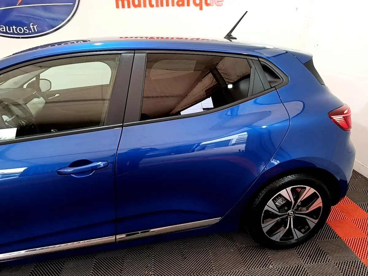 Profil côté gauche d'une Renault Clio bleu 2022 avec jantes alliage et poignées de porte ton caisse.