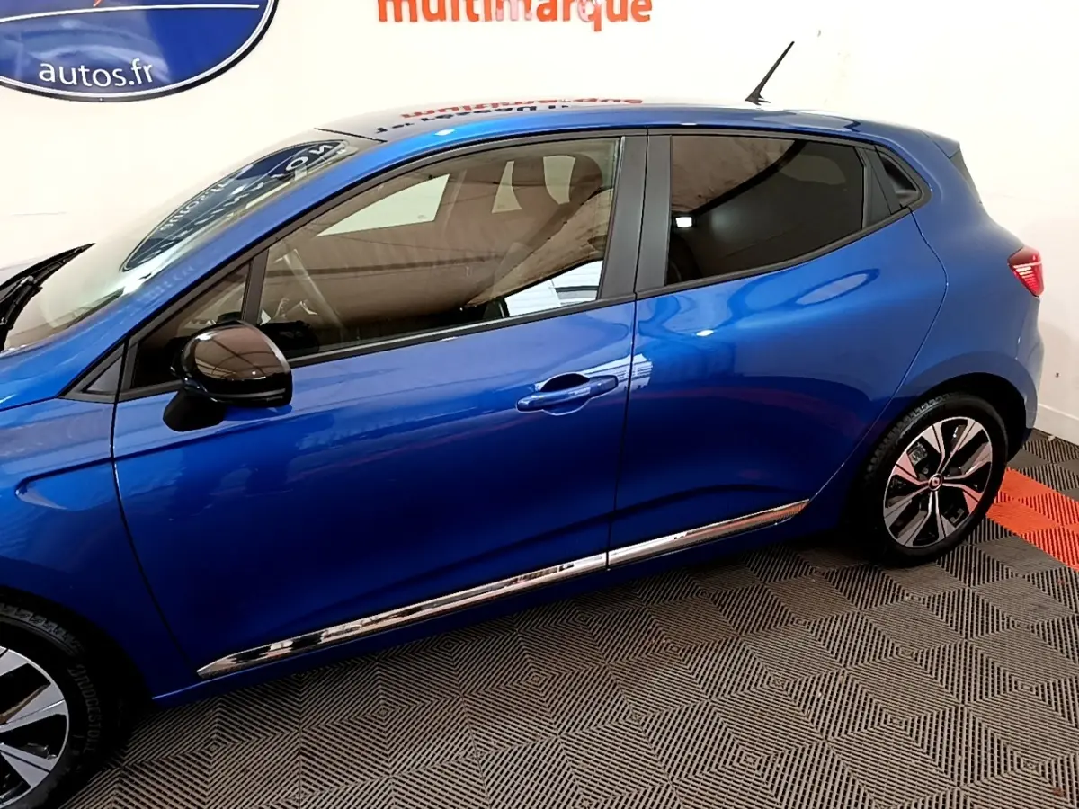 Profil droit d'une Renault Clio Evolution bleu 2022 avec rétroviseurs noirs et jantes stylisées en intérieur showroom.