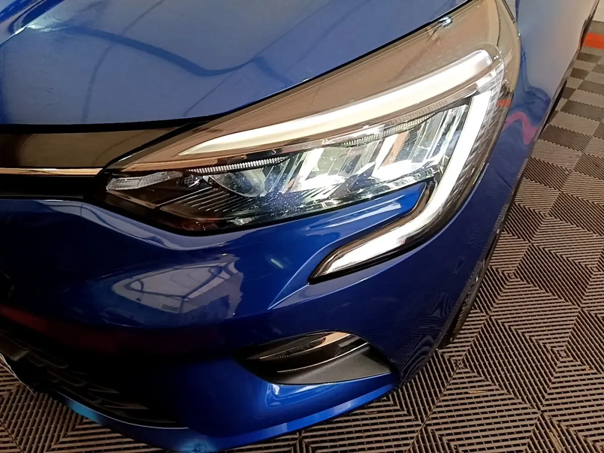 Gros plan sur le phare avant droit de la Renault Clio Evolution bleu, mettant en valeur les feux LED et la carrosserie brillante.