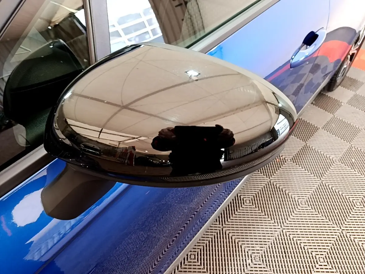 Rétroviseur droit noir brillant d’une Renault Clio bleu, vue rapprochée côté passager.