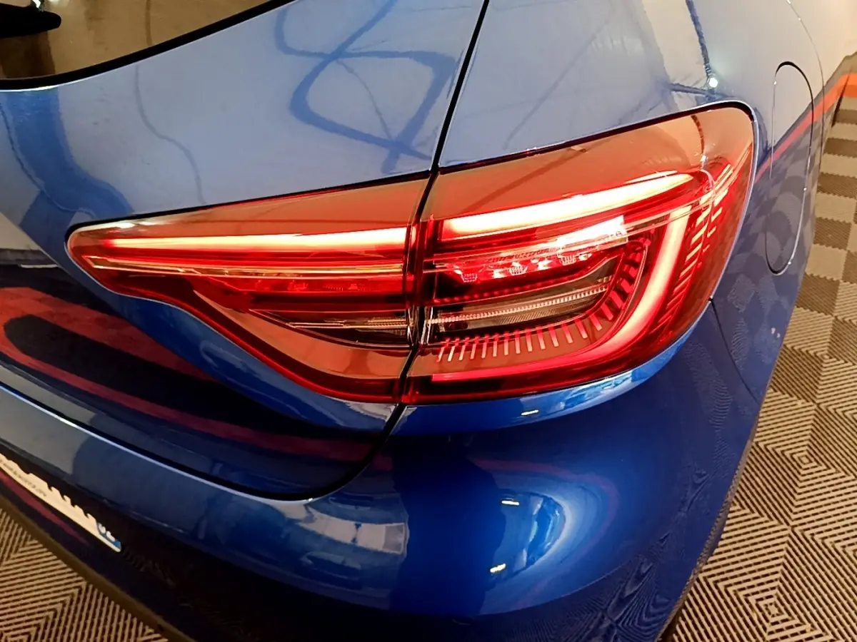 Gros plan sur le feu arrière droit rouge d’une Renault Clio bleu électrique, avec la carrosserie brillante visible autour.