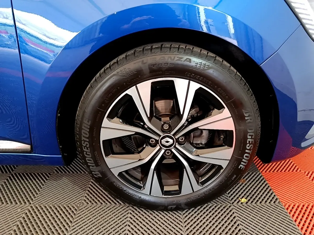 Gros plan sur la roue avant droite d’une Renault Clio bleu 2022 avec jante alliage bicolore et logo Renault central.