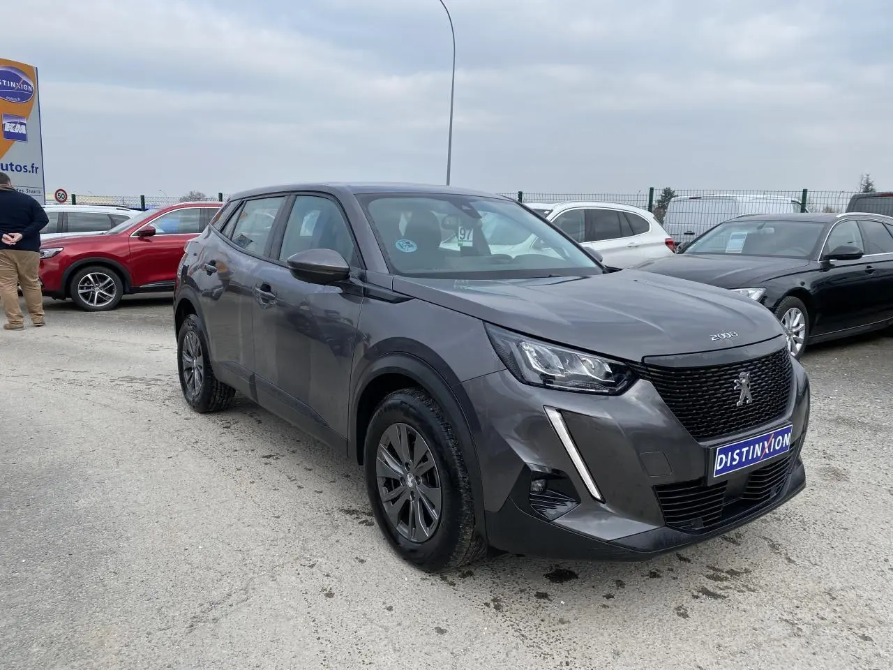 Peugeot 2008 gris foncé en 3/4 avant droit, avec calandre noire et feux LED distinctifs visibles.