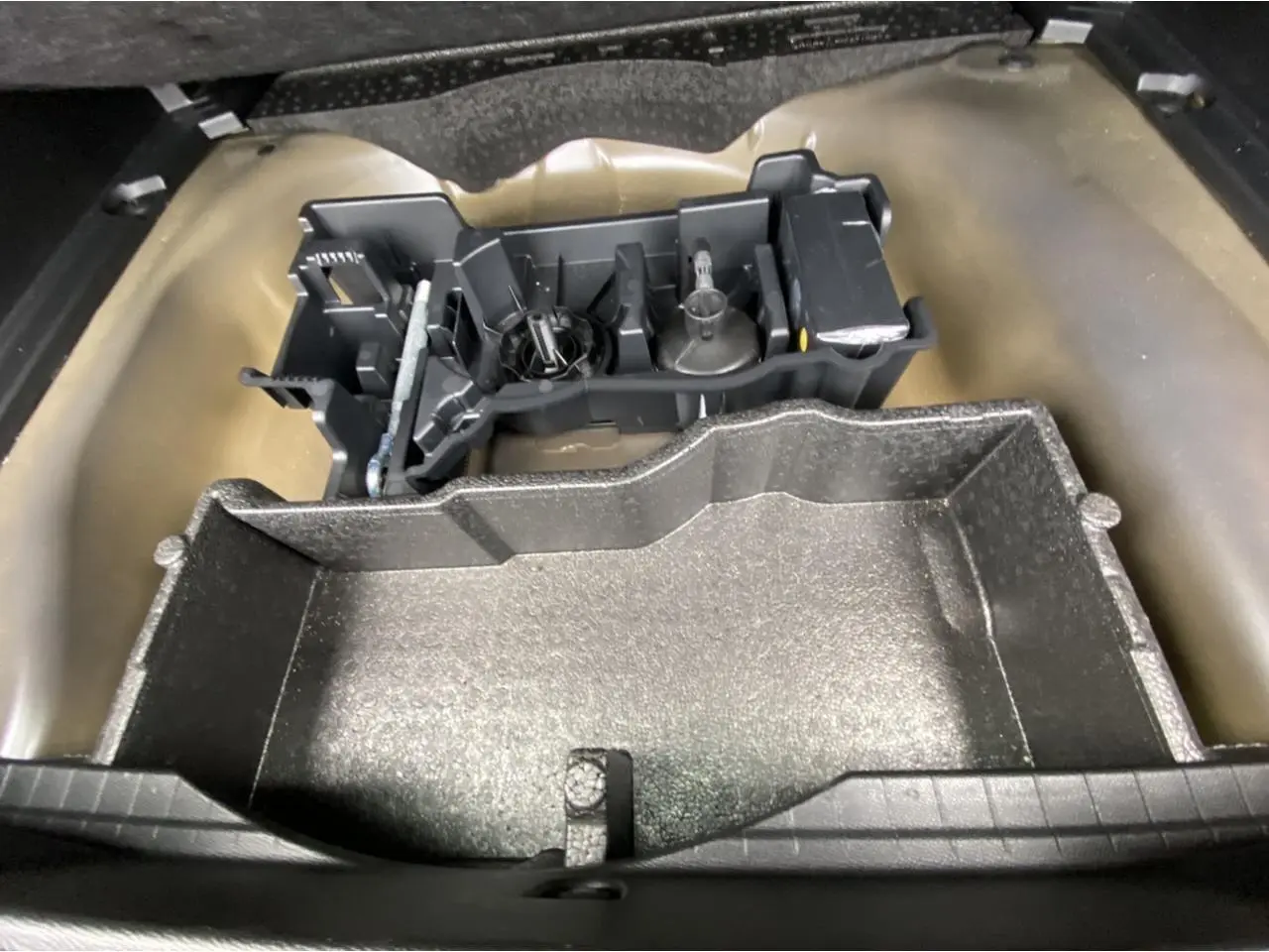Coffre ouvert d’une Peugeot 2008 gris foncé, montrant le rangement sous plancher avec outils de bord.