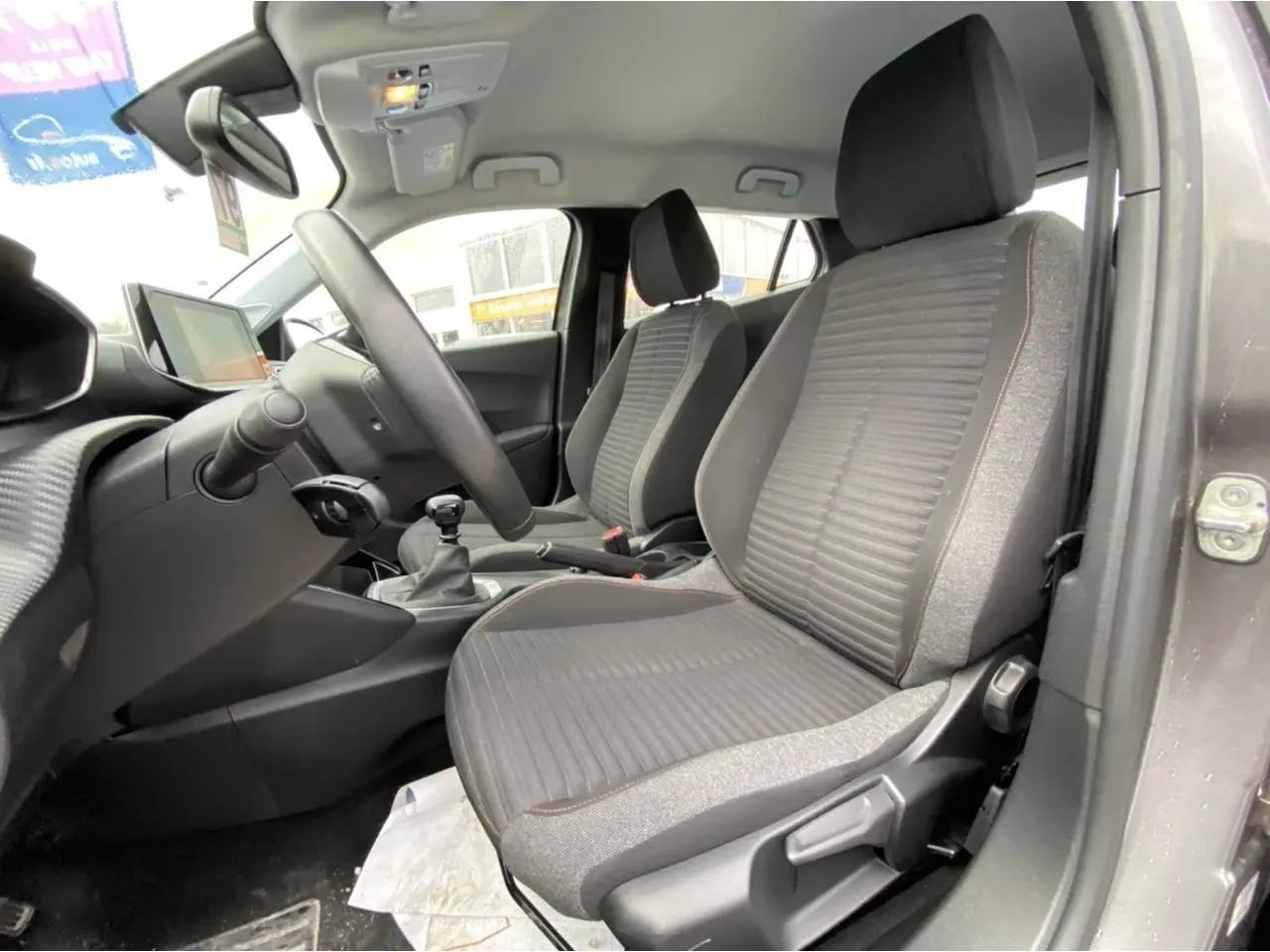 Vue intérieure côté conducteur de la Peugeot 2008 gris foncé, montrant les sièges avant et le volant avec boîte manuelle.