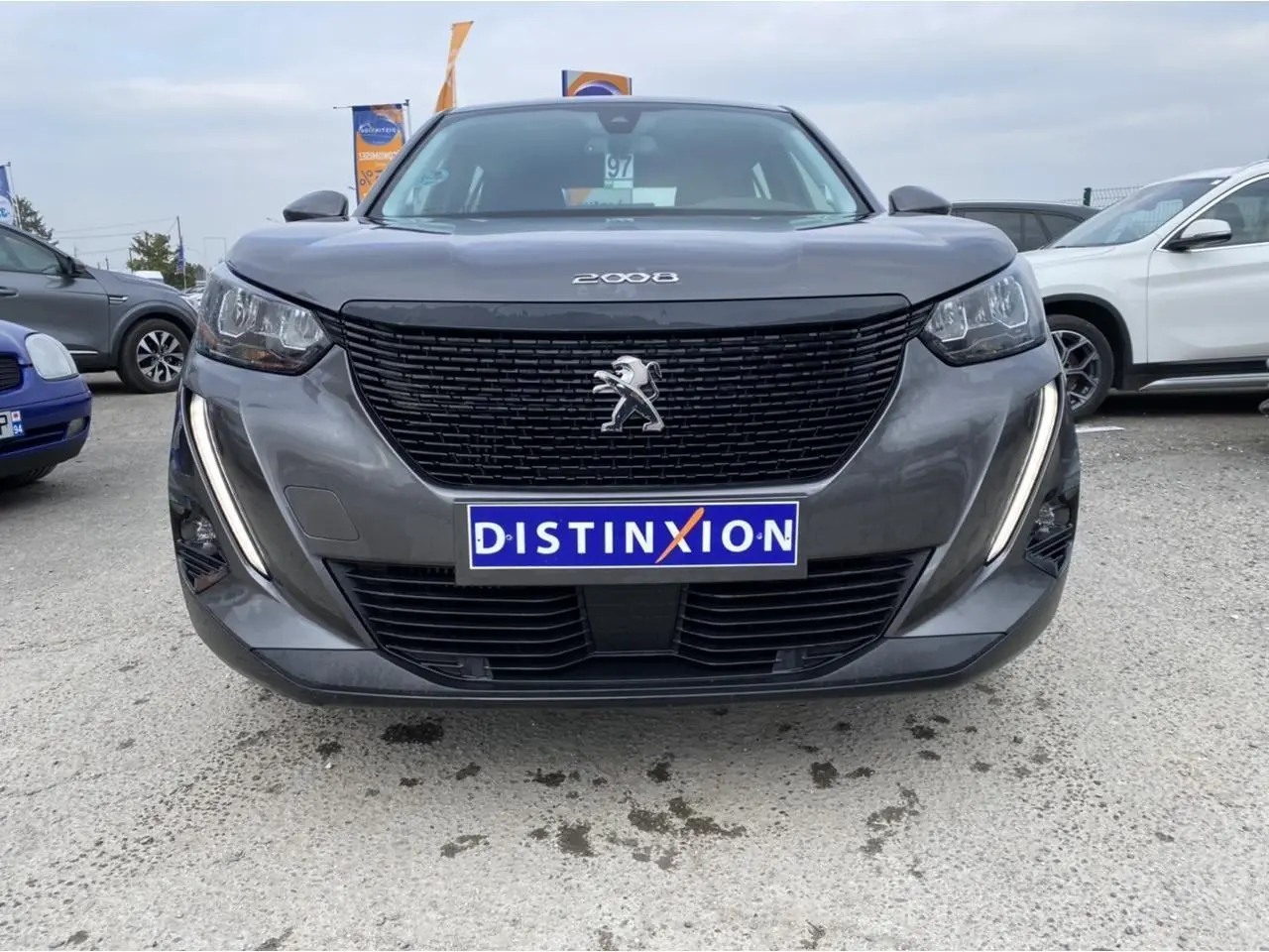 Vue frontale d'un Peugeot 2008 gris foncé avec calandre noire et feux LED en forme de griffes allumés.