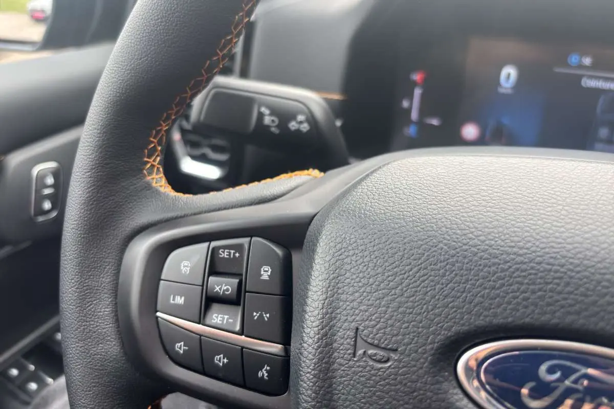 Gros plan sur le volant cuir noir du Ford Ranger Wildtrak 2026, avec commandes multifonctions et surpiqûres orange.