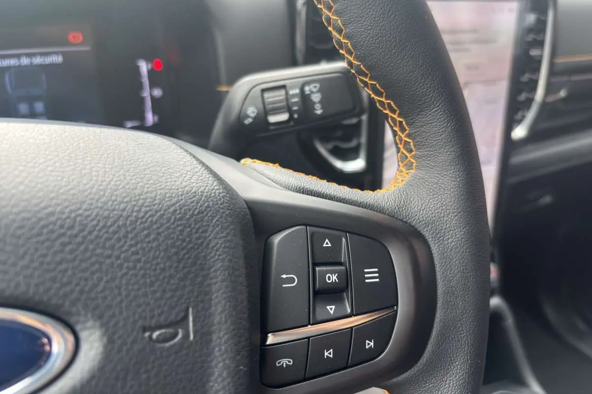 Gros plan sur le volant cuir noir avec surpiqûres orange du Ford Ranger Wildtrak 2026, boutons multifonctions visibles.