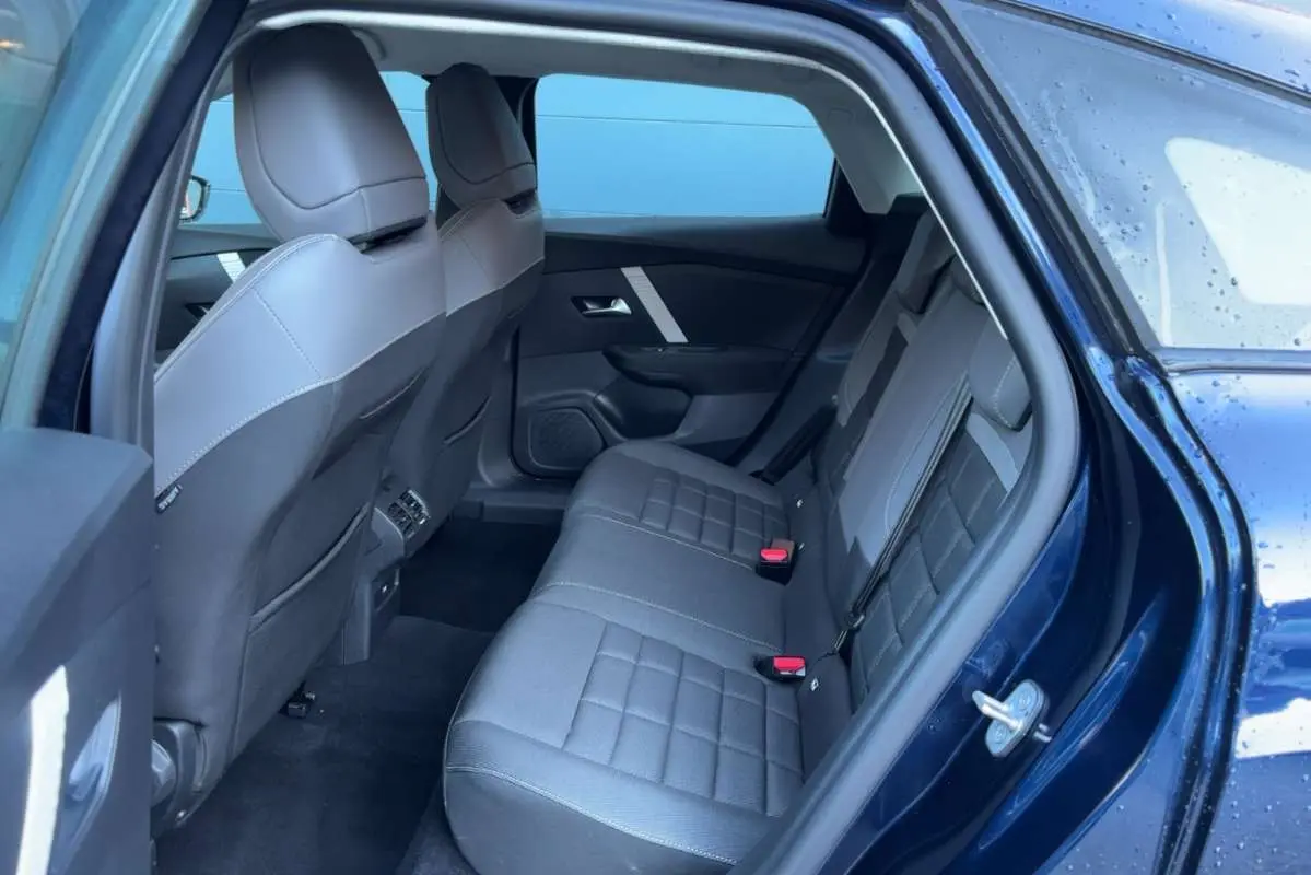 Vue côté droit de l'habitacle arrière d'une Citroën C4 hybride 2025 bleu eclipse, sièges tissu gris avec surpiqûres.