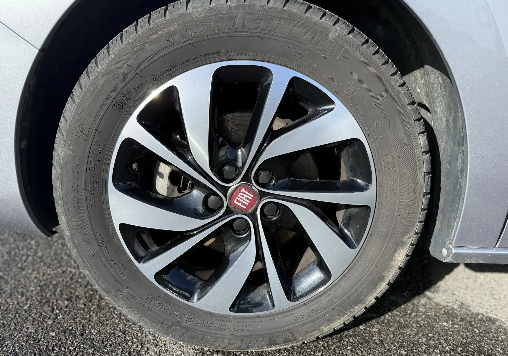 Gros plan sur la roue avant droite du FIAT Scudo gris, mettant en valeur la jante bi-ton et le logo central rouge.